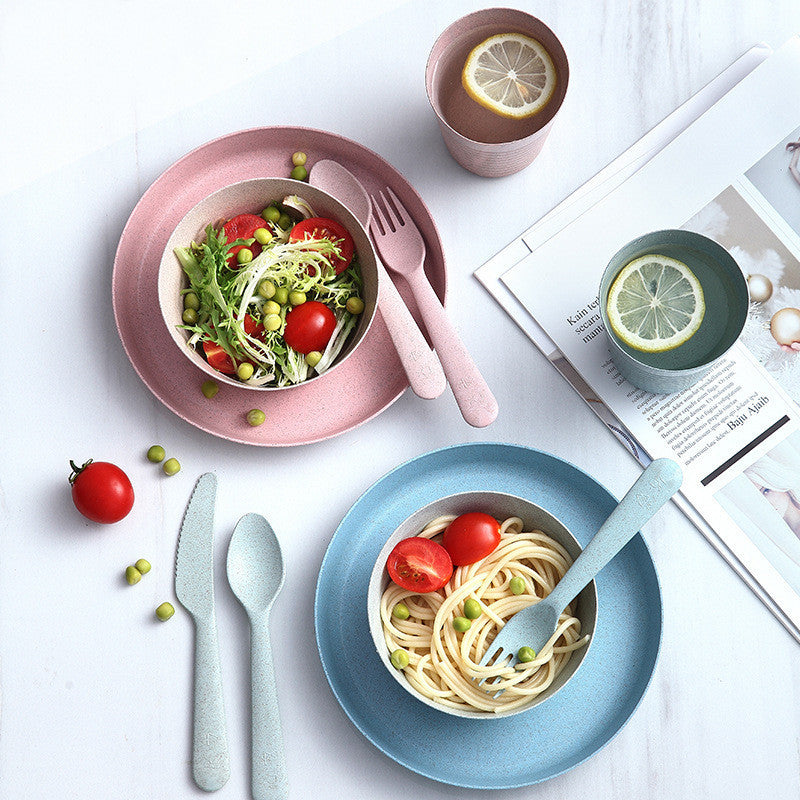 mage showing an eco-friendly wheat straw cutlery and dishware set packaged in kraft cartons. The set includes dual-color (pink and green) knives, spoons, and forks, as well as matching cups, bowls, and plates, all designed with a modern, minimalist aesthetic and built for drop-proof durability
