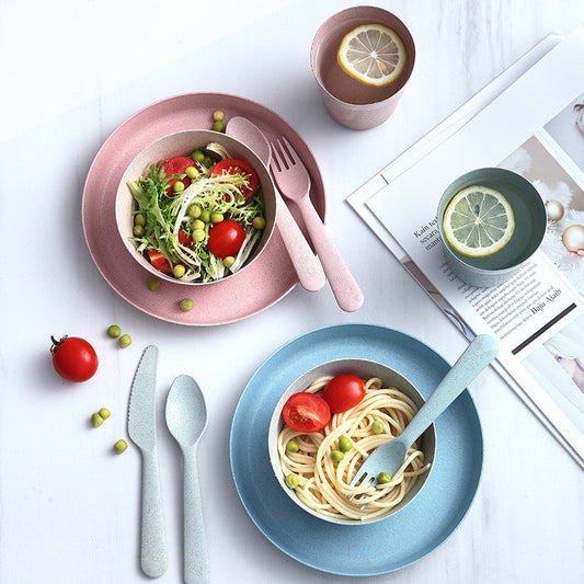 mage showing an eco-friendly wheat straw cutlery and dishware set packaged in kraft cartons. The set includes dual-color (pink and green) knives, spoons, and forks, as well as matching cups, bowls, and plates, all designed with a modern, minimalist aesthetic and built for drop-proof durability